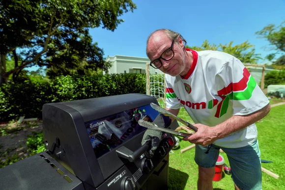 Eine Person mit Brille und Sporttrikot blickt im Garten neugierig in die Kamera.